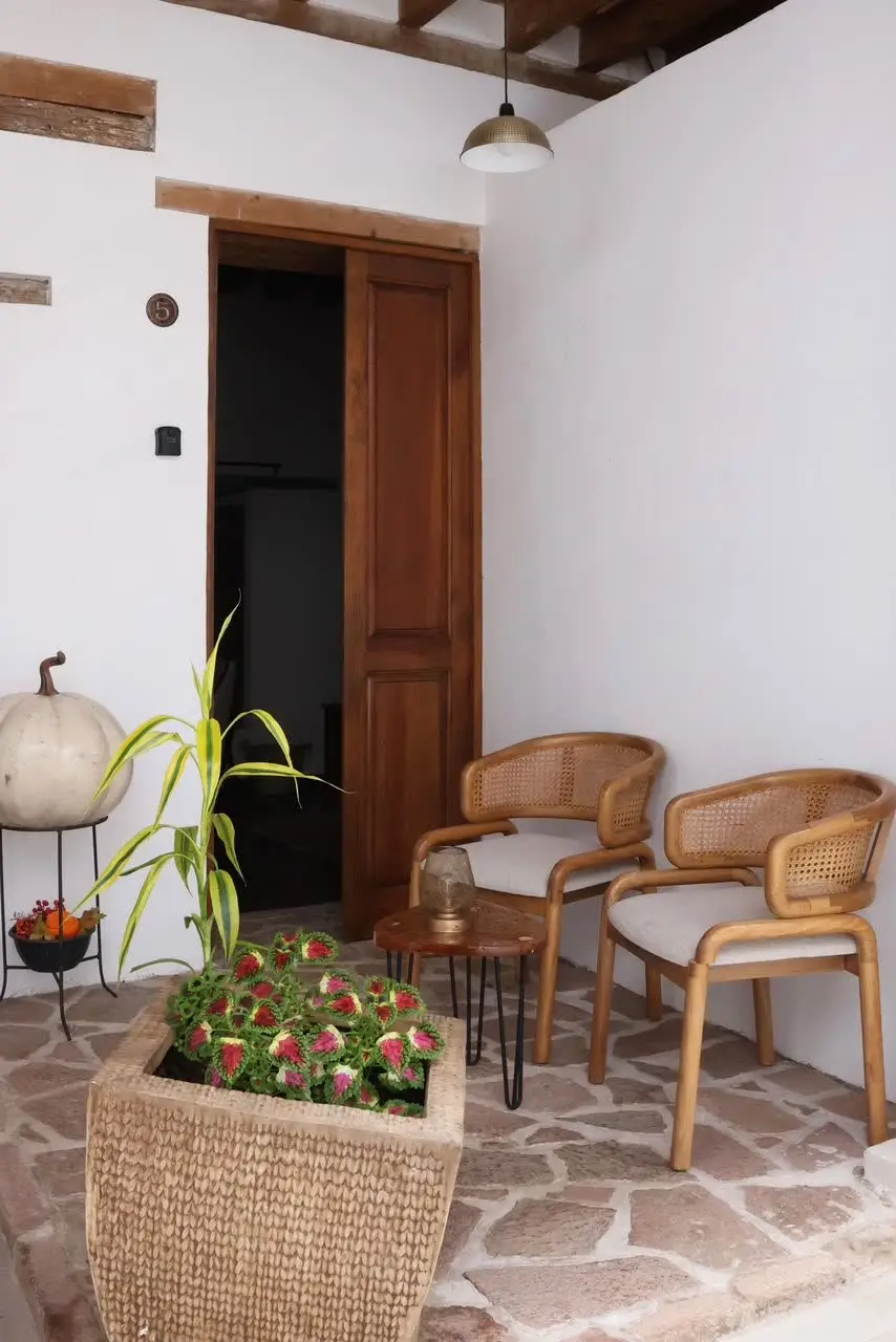 Rincón de estar exterior con sillas de ratán junto a una entrada